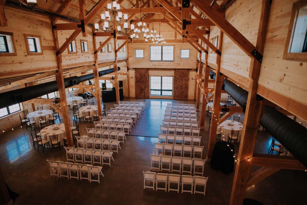 A view of the beautiful interior of the event hall, as seen from the ceiling. Gorgeous hanging light strings illuminate elegantly arranged and decorated tables and chairs, to a foreground of wooden interior.